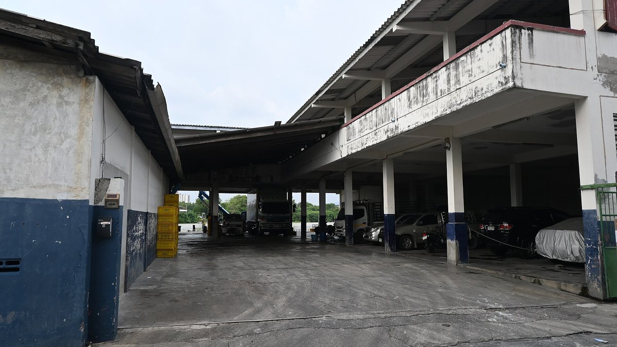 DFC 2163 A covered parking and service area beneath a weathered two-story building with several parked cars and an open concrete driveway