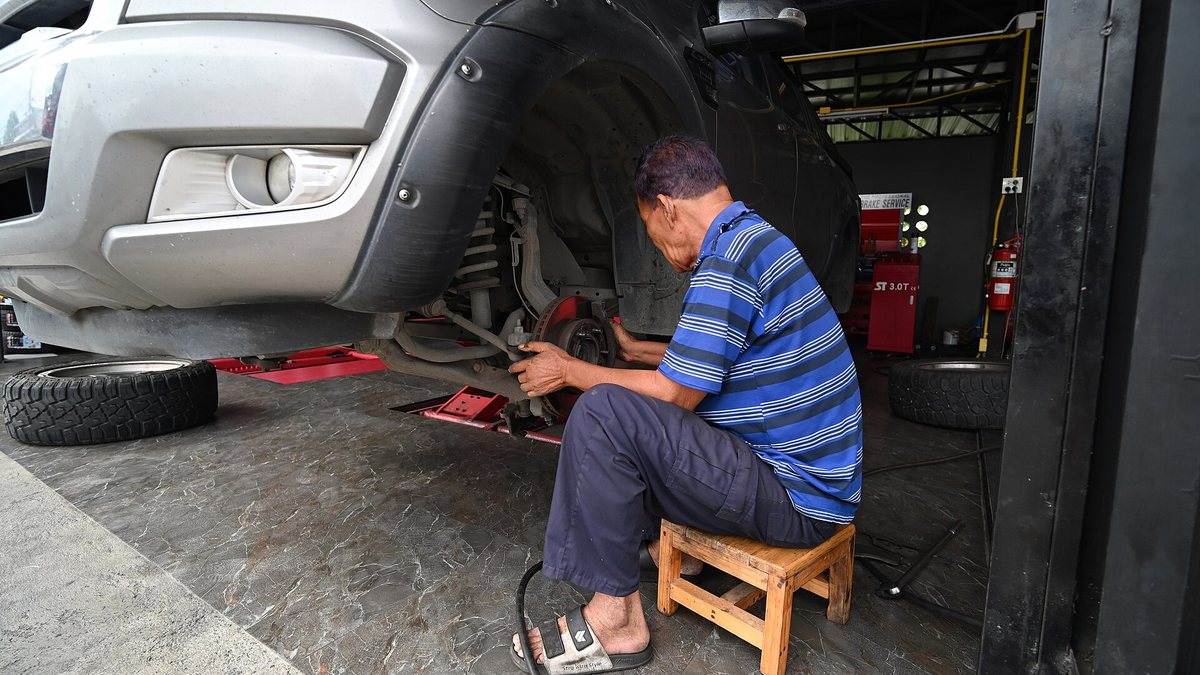 DSC 6745 A mechanic sitting on a small wooden stool working on the front suspension of a raised pickup truck in a garage