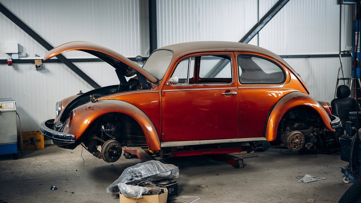 Classic car restoration project taking place in a garage with focus on an orange Beetle car